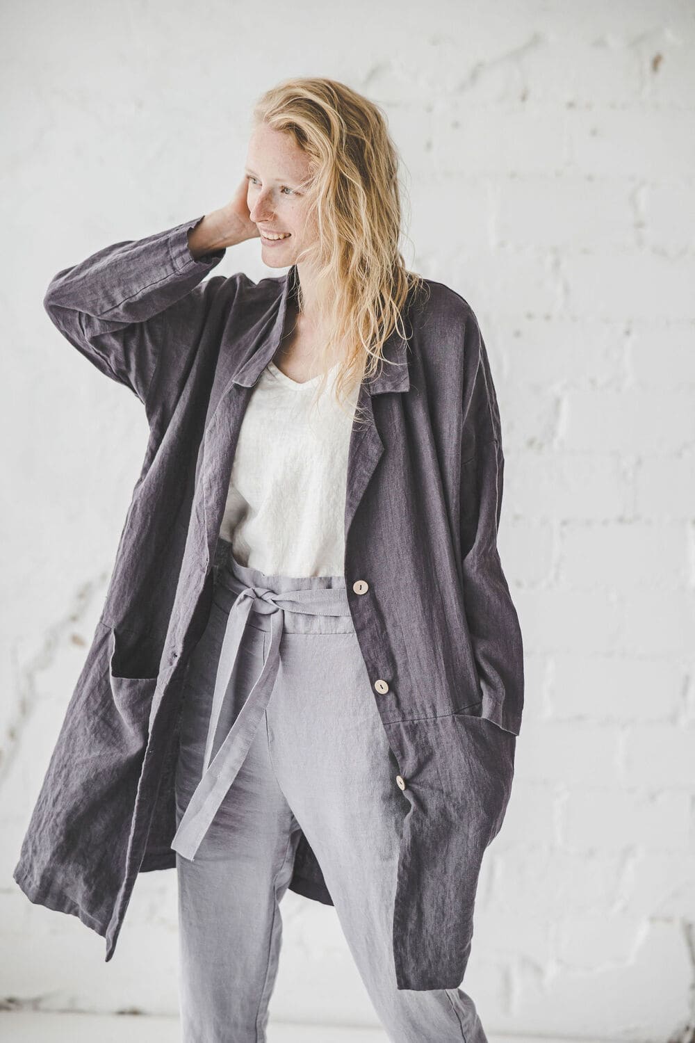 Woman wearing a long dark linen coat over a light linen outfit against. Epic Linen