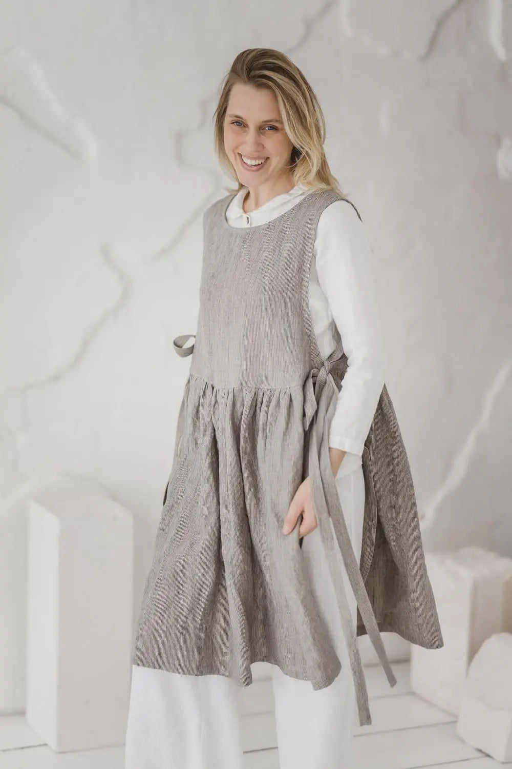 Woman holding side ties of Convertible Linen Pinafore Dress - Epic Linen