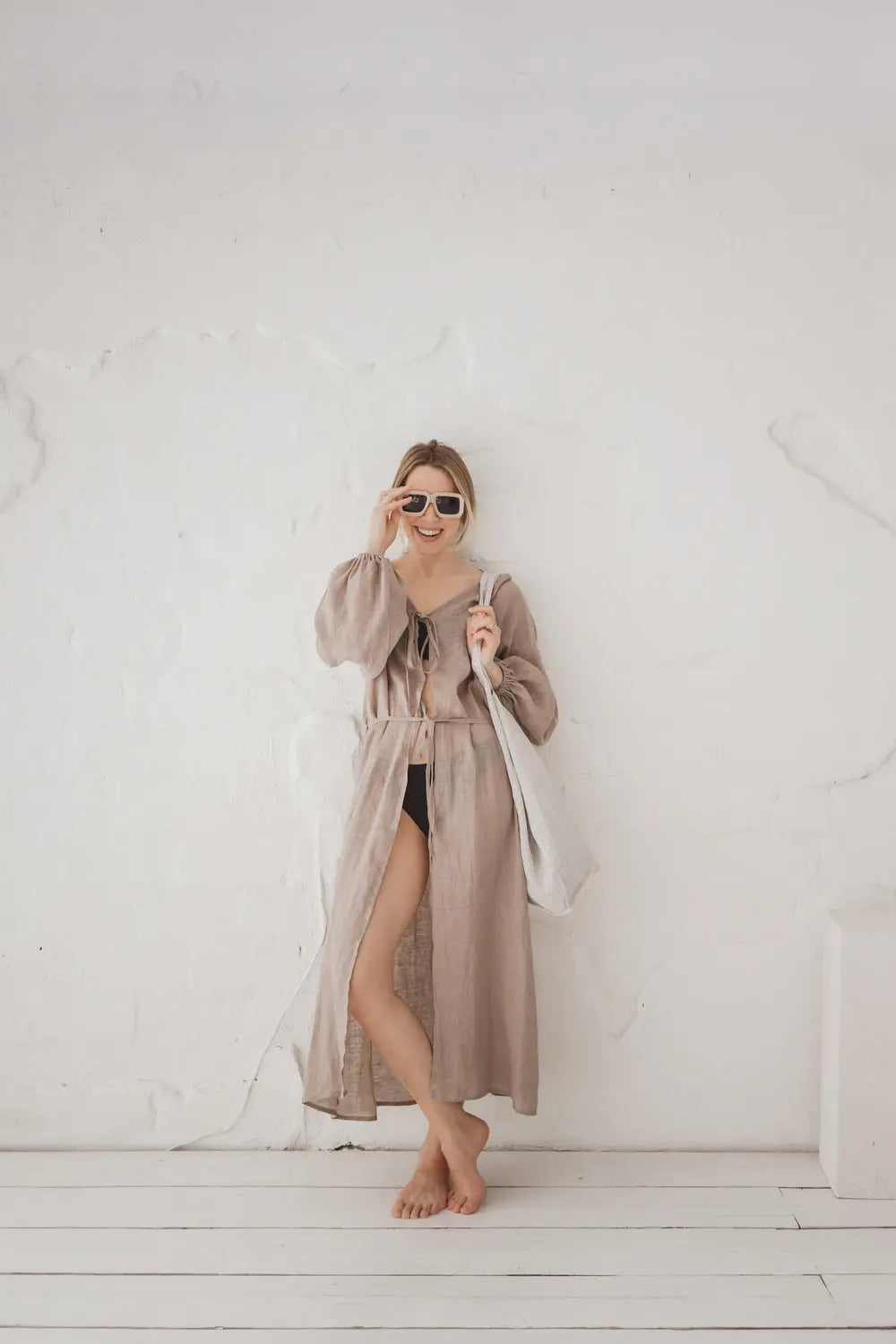 Woman wearing a flowing natural linen kaftan with long sleeves and waist tie, full length front view