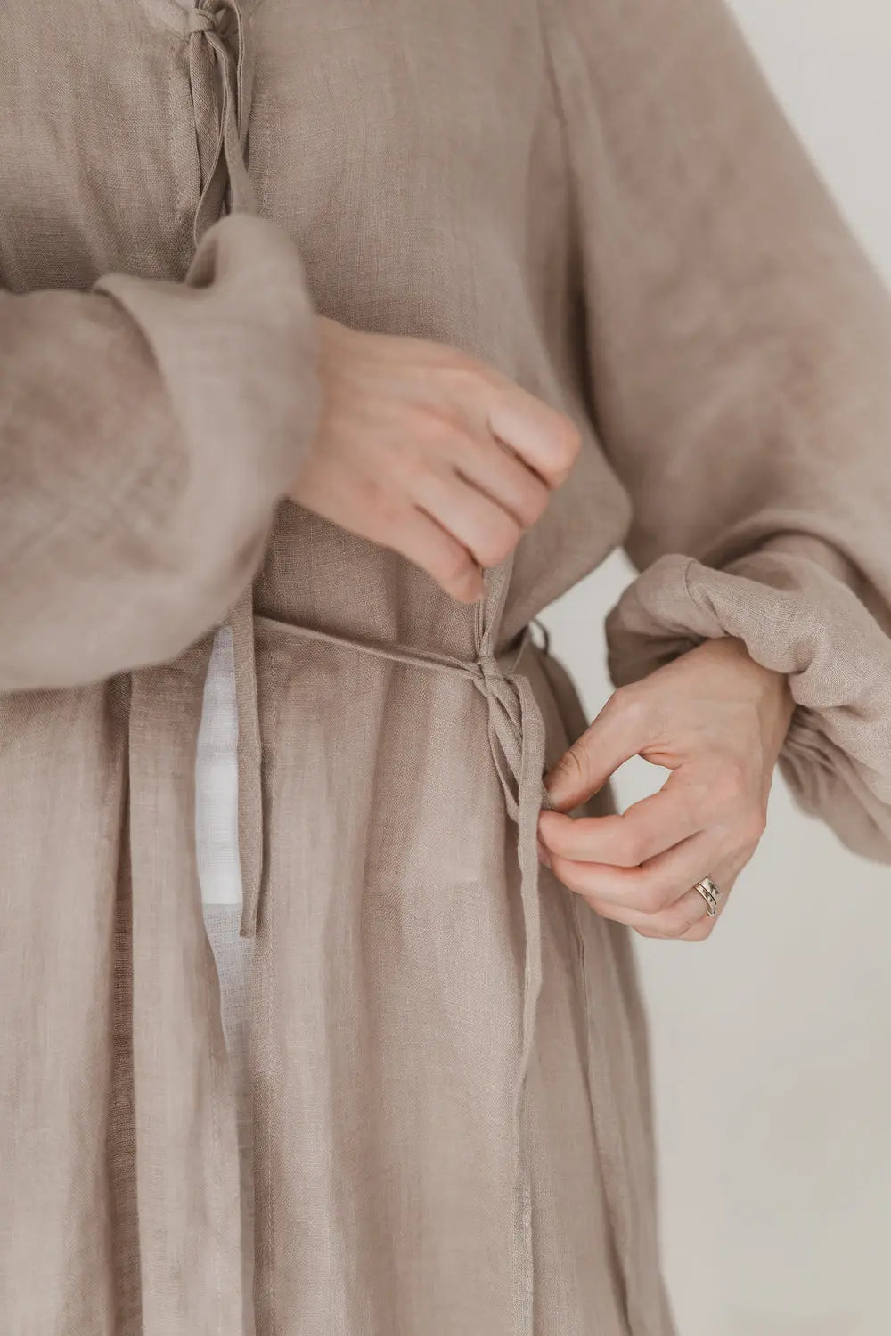 Close-up of hands tying the waist tie on a natural linen kaftan