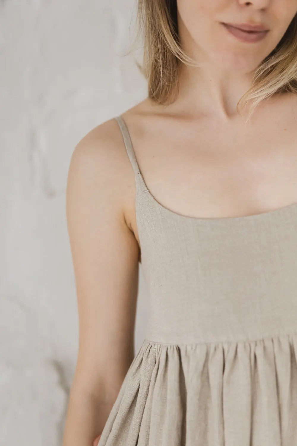 Close-up detail of scoop neckline, spaghetti straps and gathered waist on a natural linen maxi dress