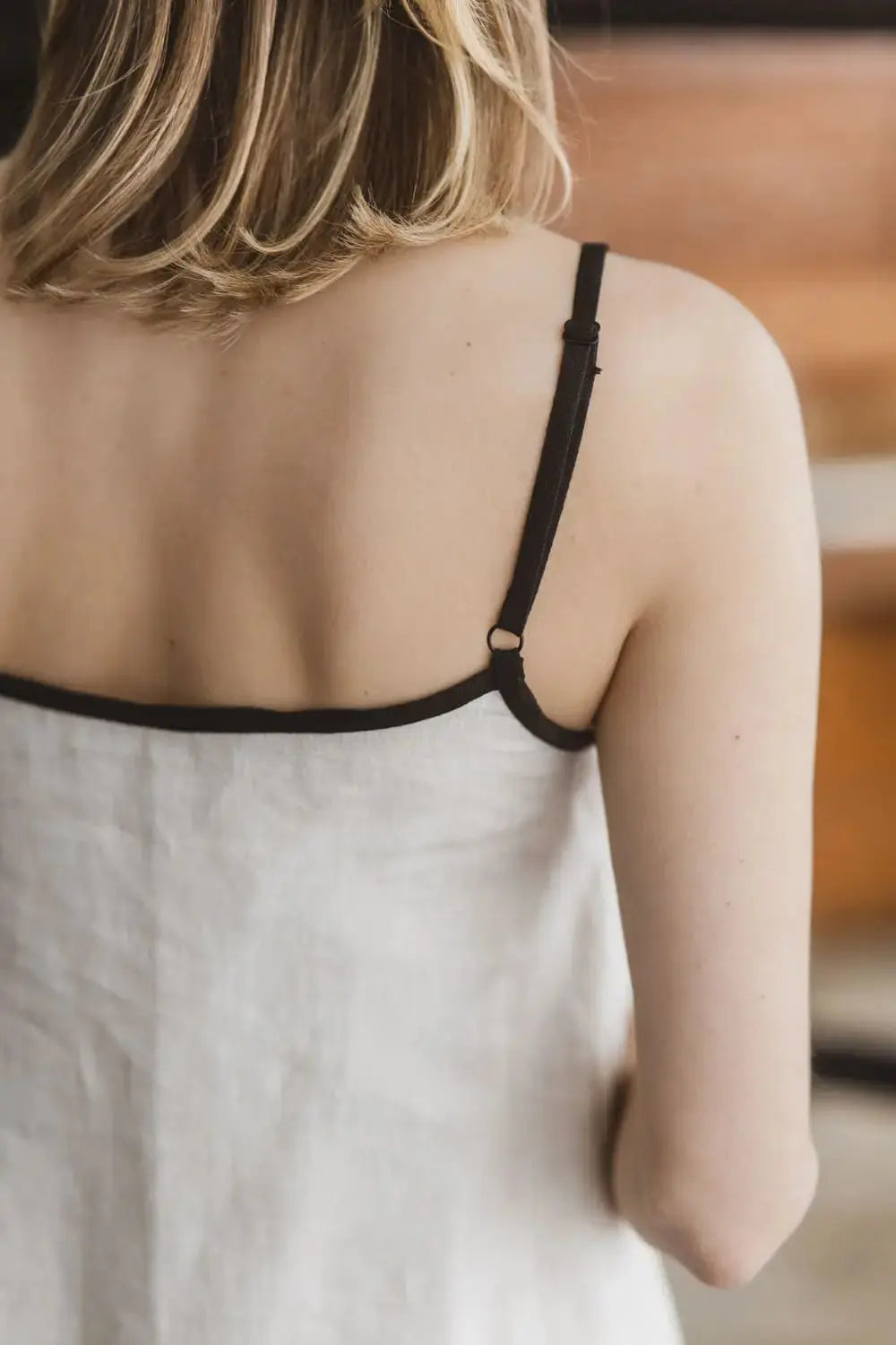 Close-up of adjustable contrast black spaghetti straps on a natural linen slip dress, back view