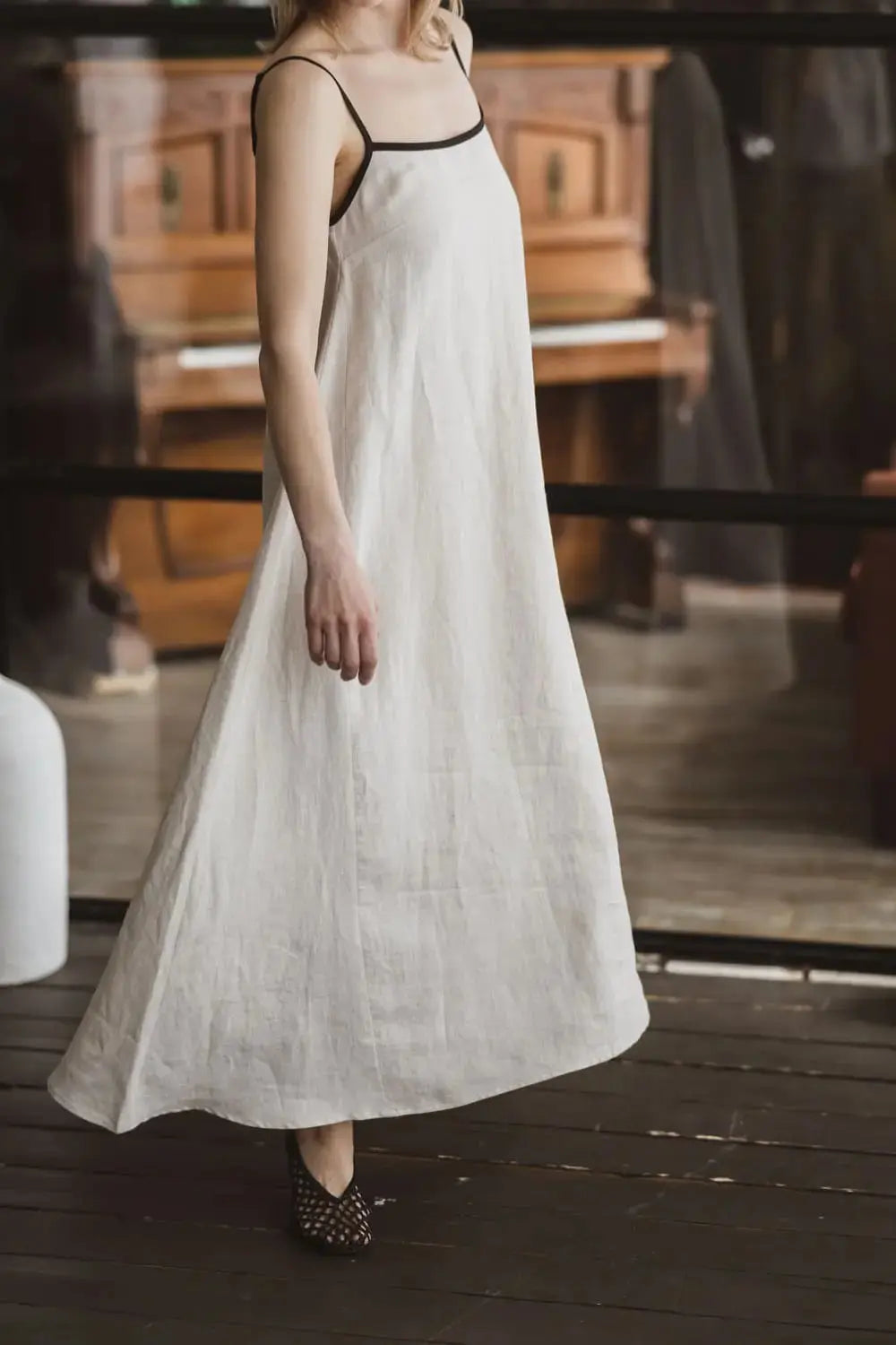 Side view of a natural linen maxi slip dress with contrast black trim and spaghetti straps, full length