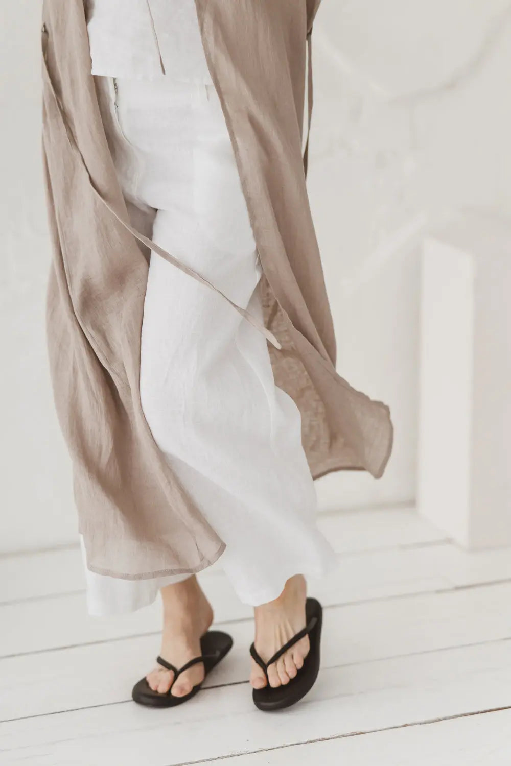 Lower half of a natural linen kaftan styled over white linen trousers with sandals